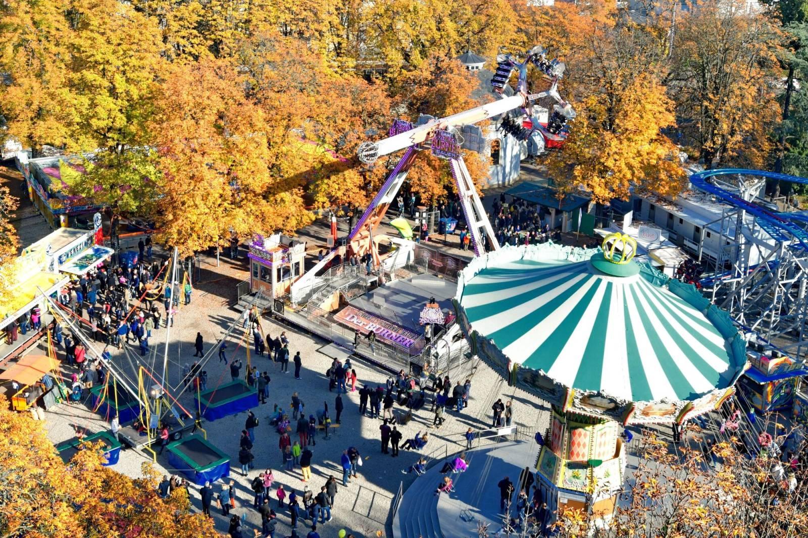 Vue d'en haut sur la Rosentalanlage, entourée d'arbres au feuillage automnal, avec un carrousel à chaînes, un trampoline et d'autres manèges.